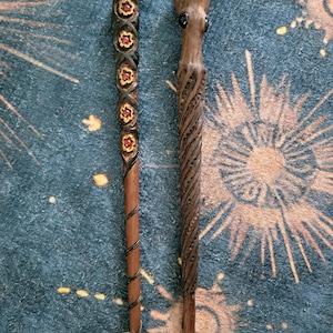 May include: Two carved wooden hair sticks. The left stick features a series of five dark-rimmed flower carvings with yellow petals and red centers, finished with a spiral wire wrap. The right stick is shaped like an octopus with dark eyes.