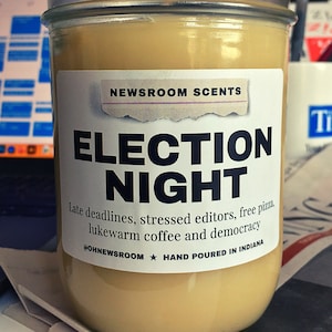 May include: A glass jar candle with a white label that reads "NEWSROOM SCENTS ELECTION NIGHT Late deadlines, stressed editors, free pizza, lukewarm coffee and democracy #OHNEWSROOM ★ HAND POURED IN INDIANA"