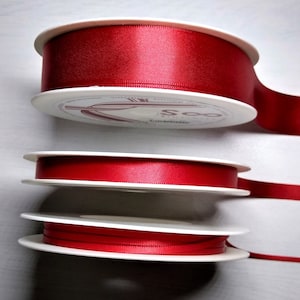 May include: Three spools of red satin ribbon, each wrapped around a white cardboard spool. The spools are stacked on top of each other.