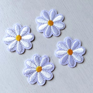 May include: Four white felt daisy flower patches with yellow centres.