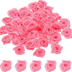 May include: A pile of small, pink satin rose embellishments. These fabric flowers have a tightly wound spiral centre and are suitable for crafting, scrapbooking, or adding a decorative touch to various projects. The roses are a vibrant shade of pink.