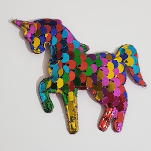 May include: A colourful rainbow unicorn applique made of sequins. The unicorn is standing on its hind legs with its head turned to the side.