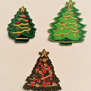 May include: Three embroidered Christmas tree patches. One is green with gold trim and red baubles, one is green with gold trim and yellow stars, and one is dark green with gold trim and red and white baubles.