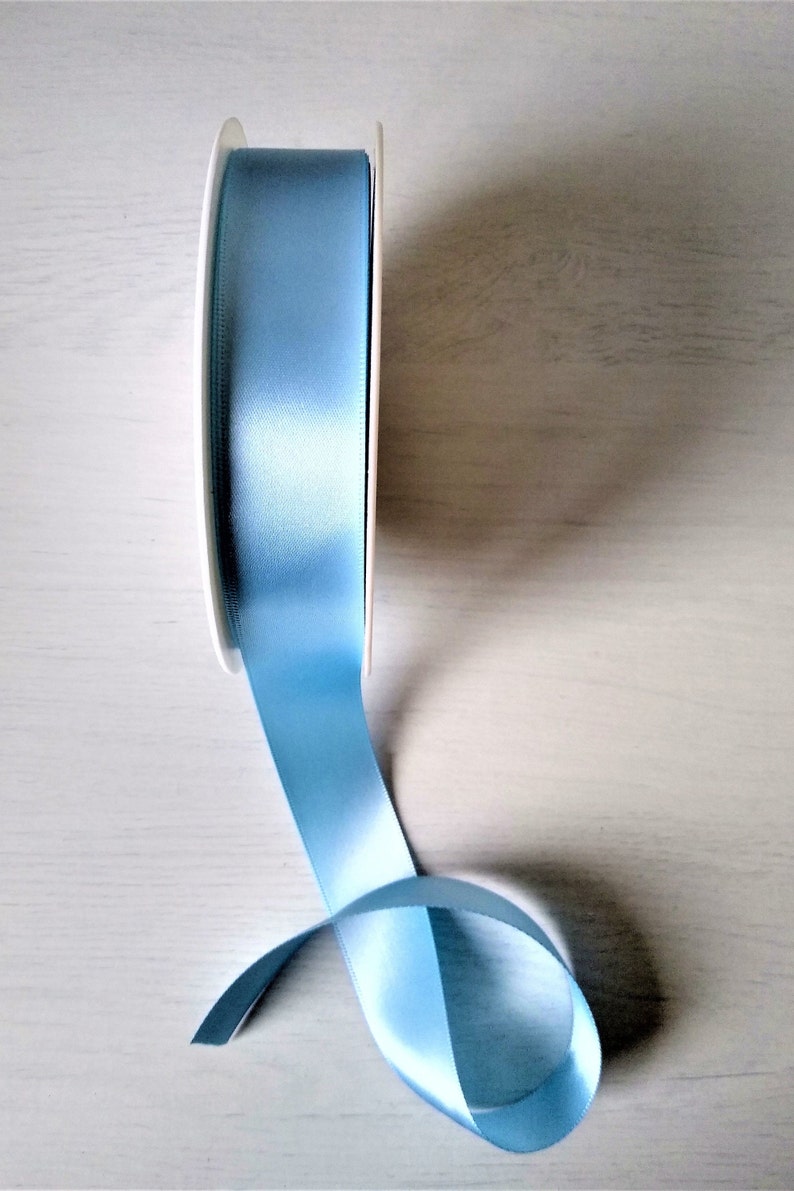 May include: A spool of light blue satin ribbon. The ribbon is wound around a white spool and is partially unwound, showing the soft, silky texture.