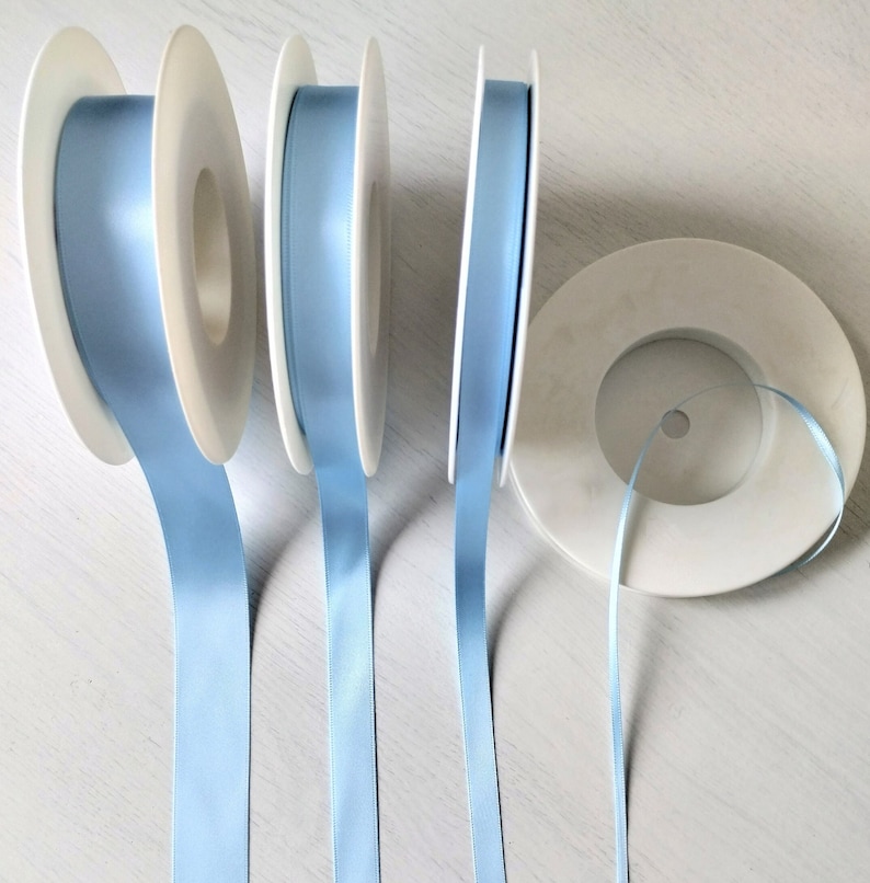 May include: Four spools of light blue satin ribbon, each wound around a white plastic spool. The ribbon is smooth and shiny.