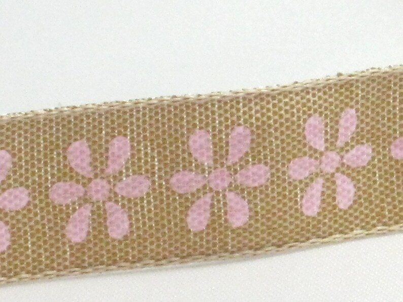 K&ouml;nnte beinhalten: Ein beigefarbenes Band mit einem sich wiederholenden Muster aus rosa Bl&uuml;ten. Das Band hat eine strukturierte, gewebte Optik.