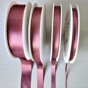 May include: Four spools of mauve satin ribbon, each with a white plastic spool. The ribbon is arranged vertically, with the spools in a row.