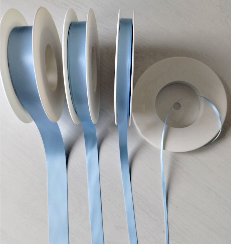 May include: Four spools of light blue satin ribbon, each wound around a white plastic spool.