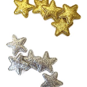 May include: A collection of gold and silver glitter star-shaped embellishments. The stars are sewn with a decorative stitch around the edges.