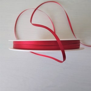 May include: A spool of red satin ribbon. The ribbon is wound around a white cardboard spool.