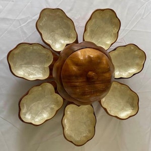 May include: A wooden serving dish shaped like a flower with six bowls. The bowls are made of mother of pearl and are attached to a central wooden base. The base has a lid that is also made of wood.