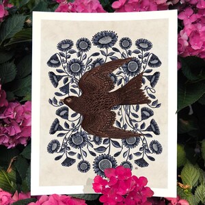 K&ouml;nnte beinhalten: Ein brauner Vogel mit ausgebreiteten Fl&uuml;geln fliegt durch einen Kreis aus blauen Blumen mit wei&szlig;en Zentren. Der Vogel ist von einem Ring aus blauen Blumen mit wei&szlig;en Zentren umgeben. Der Hintergrund ist cremefarben.