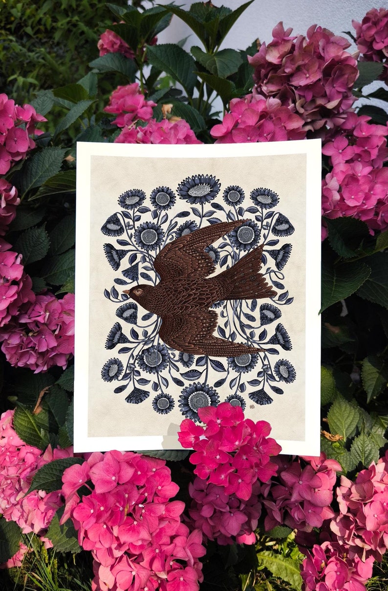 K&ouml;nnte beinhalten: Ein brauner Vogel mit ausgebreiteten Fl&uuml;geln fliegt durch einen Kreis aus blauen Blumen mit wei&szlig;en Zentren. Der Vogel ist von einem Ring aus blauen Blumen mit wei&szlig;en Zentren umgeben. Der Hintergrund ist cremefarben.