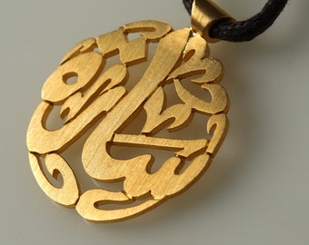 May include: A gold pendant necklace with a circular design featuring intricate Arabic calligraphy.
