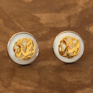 May include: A pair of gold and white earrings with a delicate, intricate design. The earrings are round and have a silver backing.