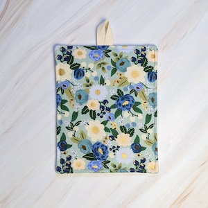 Puede incluir: Un agarrador de olla de cocina con estampado floral azul claro y blanco con un lazo de colgar de color crema.