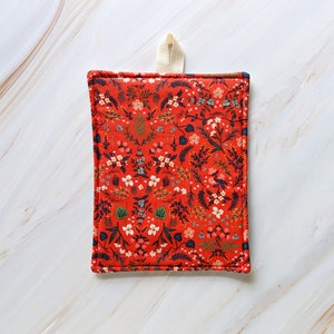Peut inclure: Un dessous de plat rouge et blanc à imprimé floral avec une boucle de suspension crème.