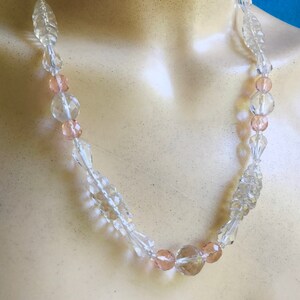 May include: A clear crystal necklace with pink crystal beads. The necklace is on a white mannequin.