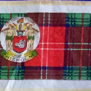 Könnte beinhalten: Ein roter, grüner und brauner Tartanstoff mit einem Wappen, das zwei Männer mit Stäben und ein Wildschwein zeigt. Das Wappen ist von einem weißen Kreis mit dem Text "By Virtue I Flourish, To The Round I Am True, Chisholm" umgeben.