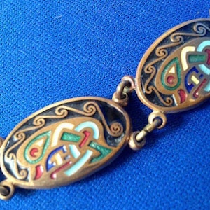 May include: A copper bracelet with two oval-shaped charms. The charms are black with intricate Celtic knot designs in green, blue, red, and white enamel.