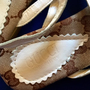May include: Close-up of the bottom of a pair of brown and white sandals with a white leather label that reads "GUCCI MADE IN ITALY".