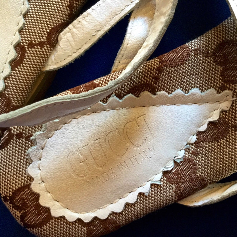 May include: Close-up of the bottom of a pair of brown and white sandals with a white leather label that reads "GUCCI MADE IN ITALY".