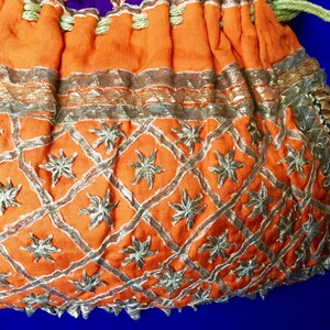 May include: Orange fabric drawstring bag with gold and silver embroidery. The bag has a geometric pattern with star-shaped designs.