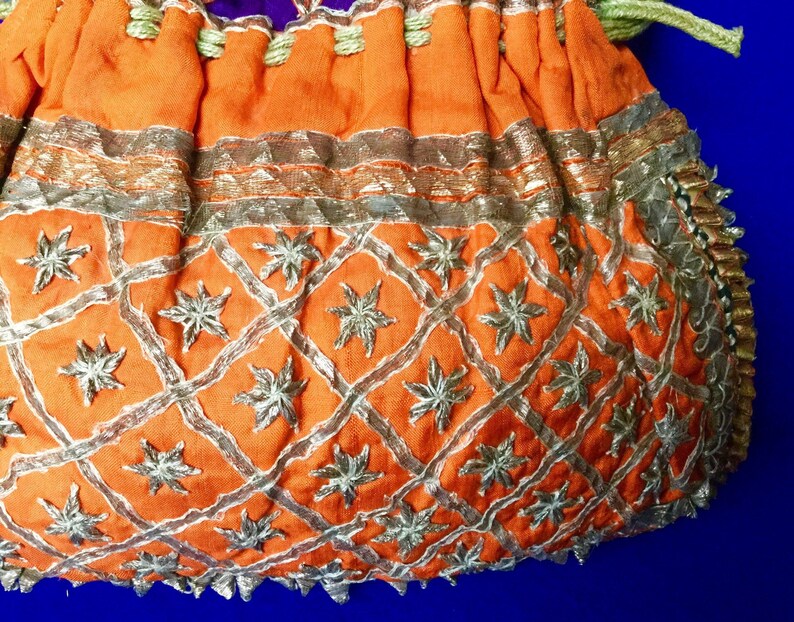 May include: Orange fabric drawstring bag with gold and silver embroidery. The bag has a geometric pattern with star-shaped designs.