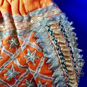 May include: A small orange drawstring bag with silver and gold embroidery. The bag has a geometric pattern with star-shaped designs and a fringed border.