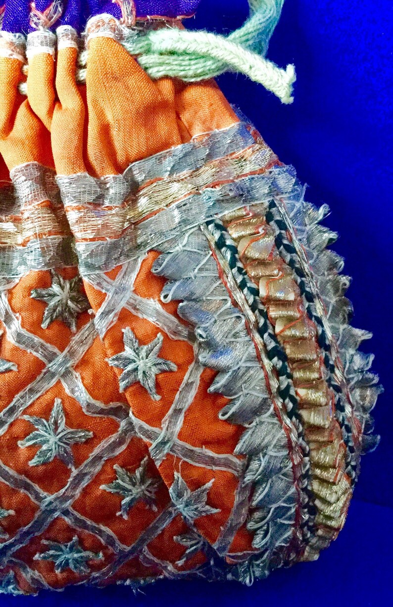 May include: A small orange drawstring bag with silver and gold embroidery. The bag has a geometric pattern with star-shaped designs and a fringed border.