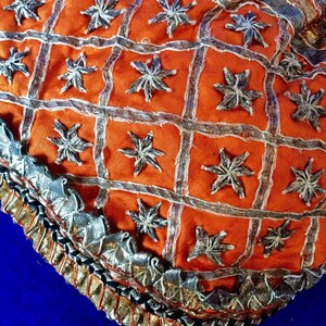 May include: Orange fabric with a silver embroidered pattern of stars. The fabric has a silver and black trim.
