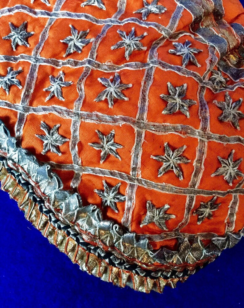 May include: Orange fabric with a silver embroidered pattern of stars. The fabric has a silver and black trim.