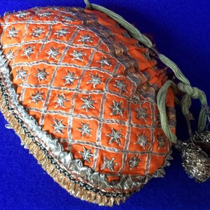 May include: An orange fabric drawstring bag with silver and gold trim. The bag is decorated with a repeating pattern of stars and has a tassel on the drawstring.