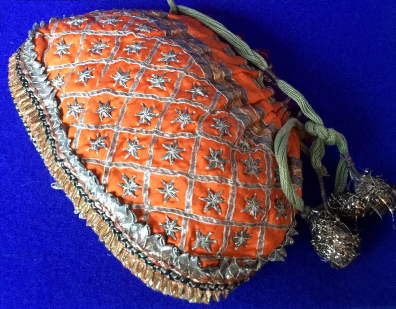 May include: An orange fabric drawstring bag with silver and gold trim. The bag is decorated with a repeating pattern of stars and has a tassel on the drawstring.