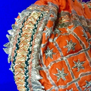 May include: A small orange drawstring bag with silver and gold embroidery. The bag has a decorative border with silver and green trim.