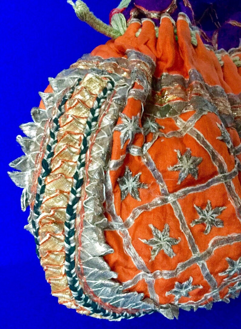May include: A small orange drawstring bag with silver and gold embroidery. The bag has a decorative border with silver and green trim.