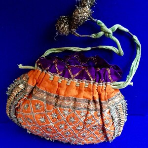 May include: A small, orange drawstring bag with a purple lining. The bag is decorated with gold and silver embroidery and beads.