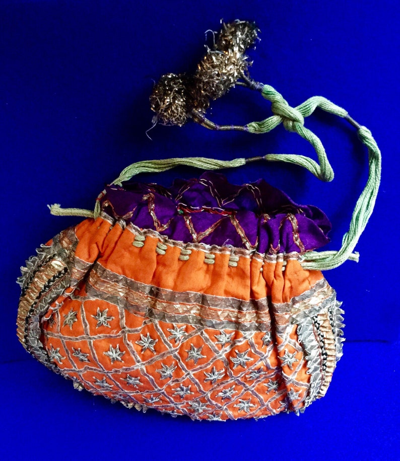 May include: A small, orange drawstring bag with a purple lining. The bag is decorated with gold and silver embroidery and beads.