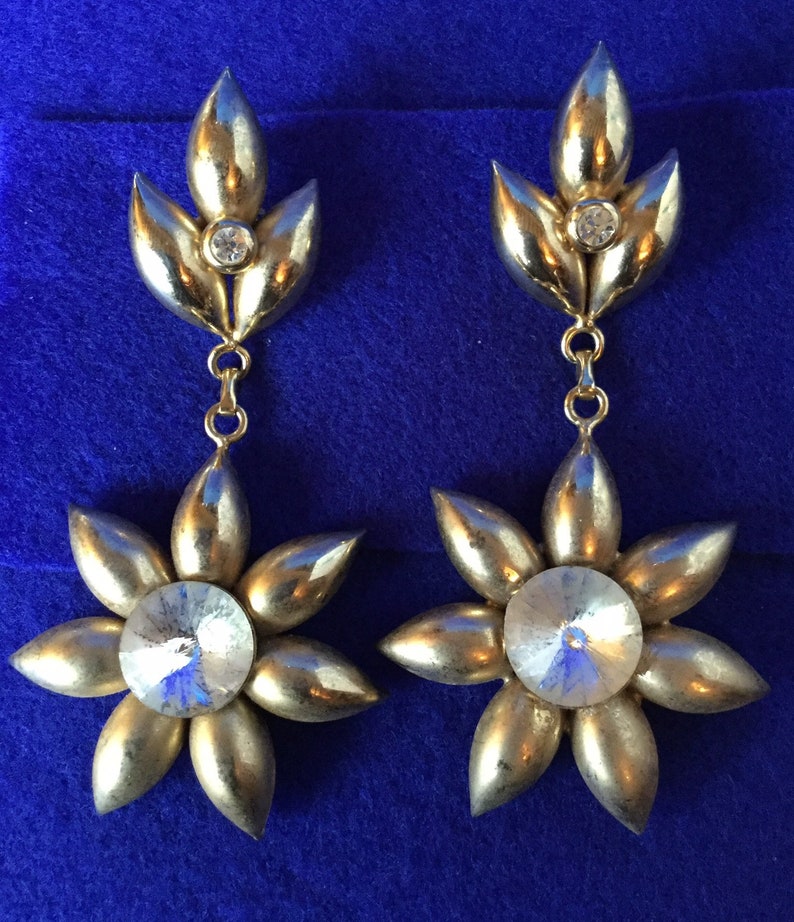 Vintage 1970s chandelier drop earrings in gold toned metal with dramatic plastic faux rhinestone centres.