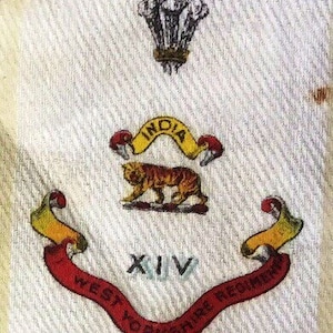 Könnte beinhalten: Ein weißer Stoffabzeichen mit einem roten, gelben und schwarzen Wappen. Das Wappen zeigt einen Tiger, eine Schriftrolle mit den Worten "West Yorkshire Regiment" und die Zahl "XIV". Das Wappen wird von einer Krone und dem Wort "INDIA" gekrönt.