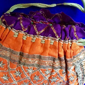 May include: A small, orange drawstring bag with gold and silver embroidery. The bag has a purple lining and a green drawstring.