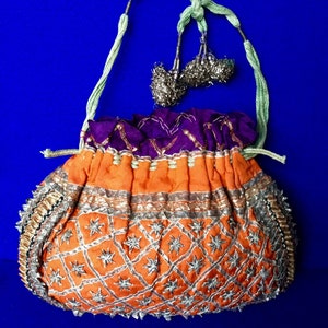 May include: A small, orange and purple drawstring bag with silver and gold embroidery. The bag has a star pattern and is decorated with beads. The bag has a green cord handle with silver tassels.