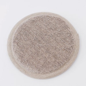 May include: A round, beige, textured, fabric pad.