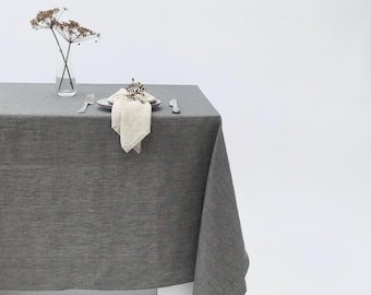 May include: A gray linen tablecloth with a white napkin and a silver napkin ring on a white table.