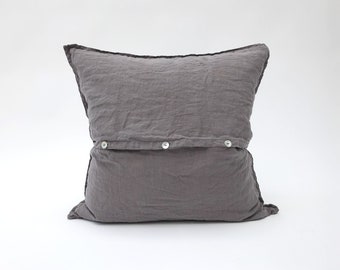 May include: A gray linen pillow with button closures. The pillow is made of a soft, natural fabric and has a relaxed, casual look.
