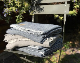 May include: A stack of four blue and gray linen throw blankets with frayed edges, sitting on a metal chair.