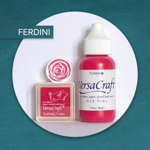 Könnte beinhalten: Ein quadratisches VersaCraft-Stempelkissen und eine Flasche Ruby K23-Tinte, beide beschriftet für Stoff, Papier und Holz. Das Stempelkissen zeigt ein Rosengrafik, und die Flasche enthält 30 ml Tinte. Der Markenname FERDINI ist oben links zu sehen.