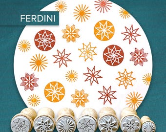 May include: A collection of wooden stamps with star and snowflake designs. The stamps are arranged in front of a white circle with matching star and snowflake patterns in orange, red, and yellow. The word "FERDINI" is in the upper left corner.