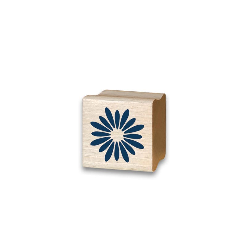 May include: A wooden stamp with a blue daisy design. The stamp is a light tan color with a curved top and sides. The daisy has a circular center with elongated petals.