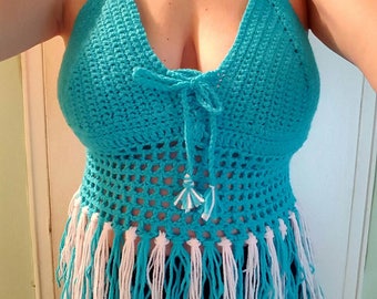 Pode incluir: Um top halter de crochê turquesa com franjas brancas. O top tem um fecho de nó na frente e enfeites decorativos nas alças.